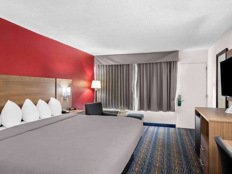 A hotel room with a large bed, a desk, a chair, a TV, and a window with curtains.