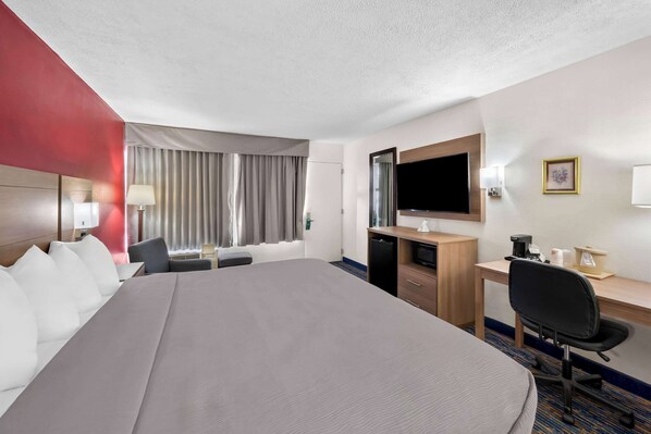 A hotel room with a large bed, a desk with a computer, a TV, and a window with curtains.