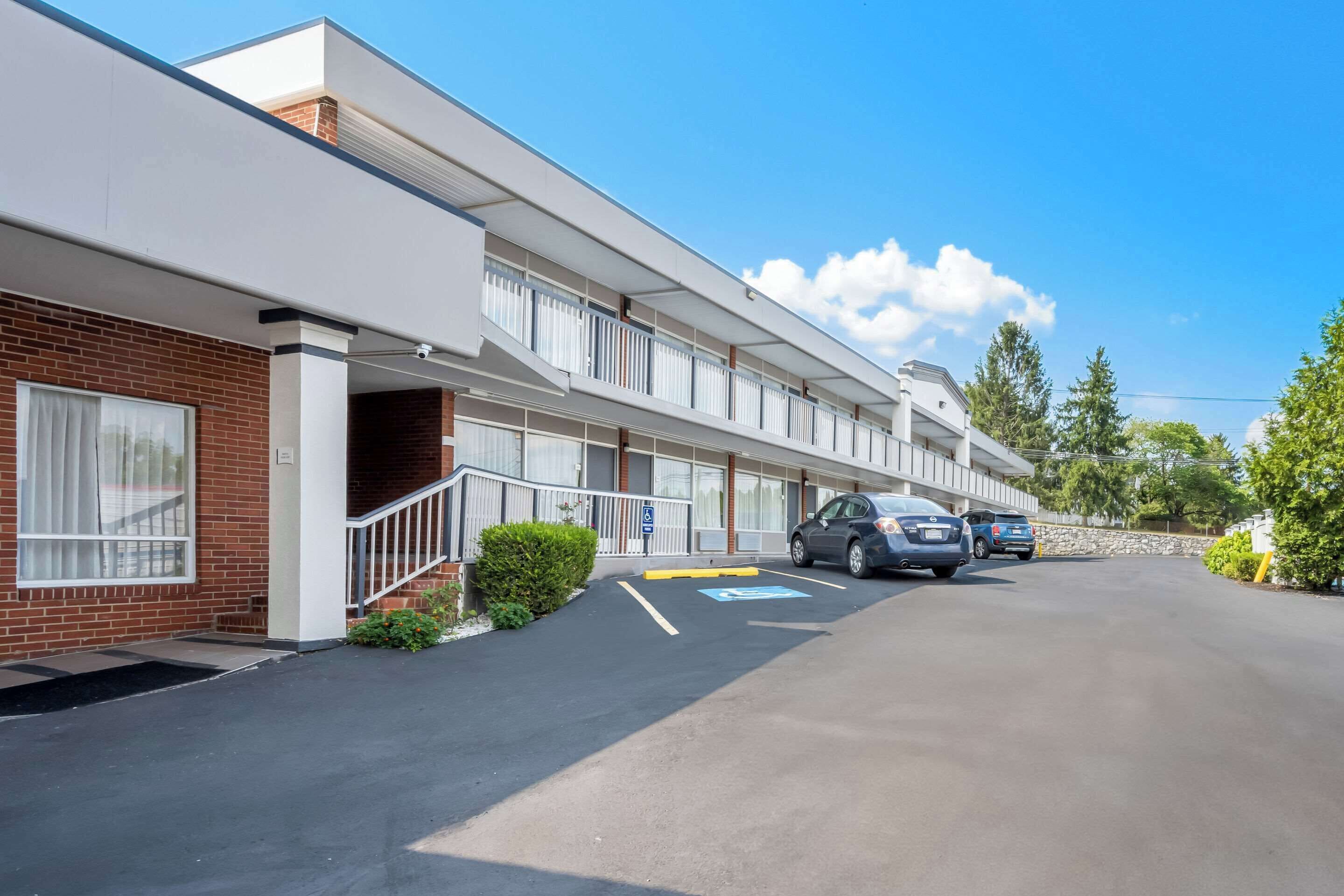 A motel with a brick facade, white exterior, and a parking lot with two cars.