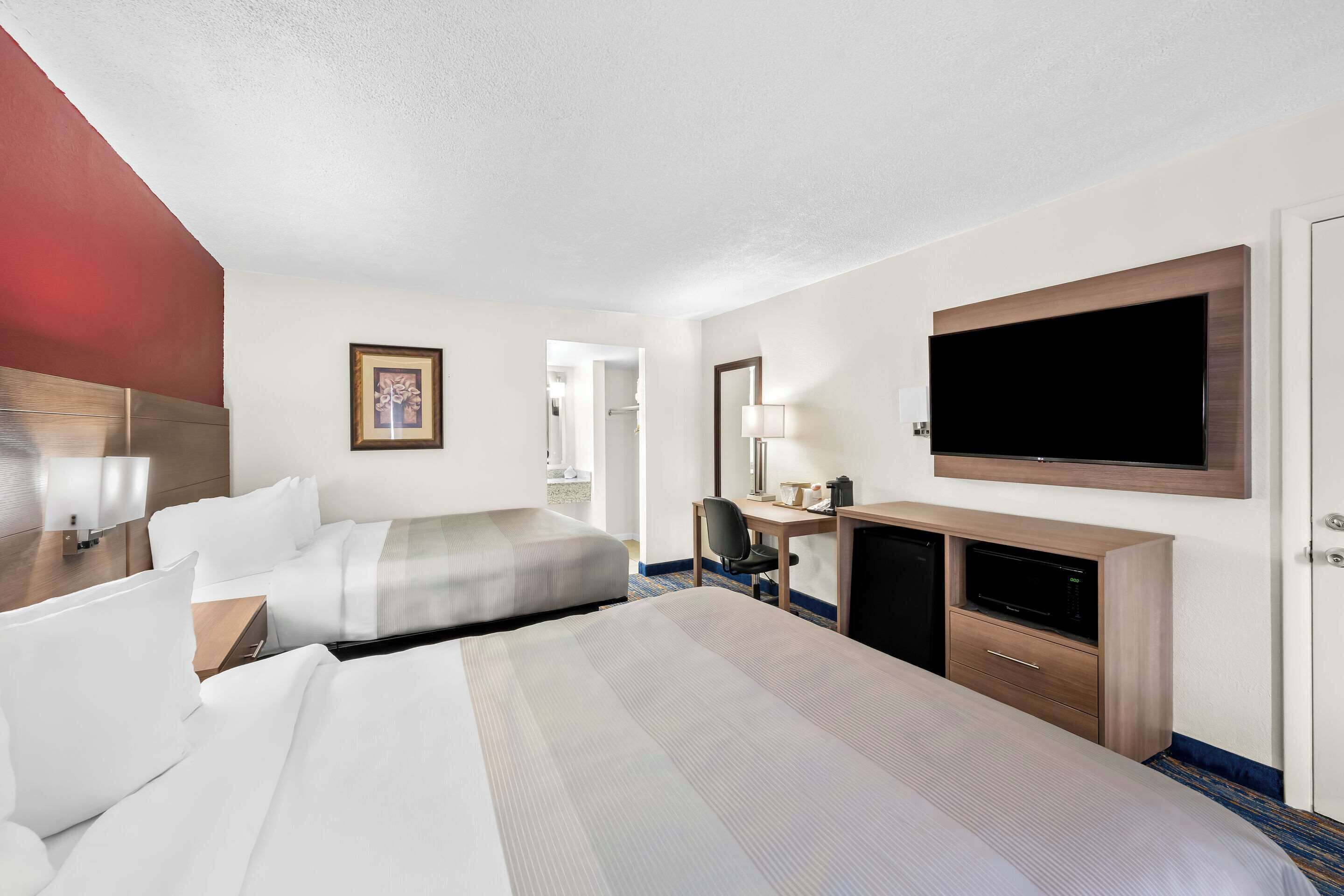 Une chambre d’hôtel avec deux lits, un bureau avec un ordinateur, une télévision et une armoire.