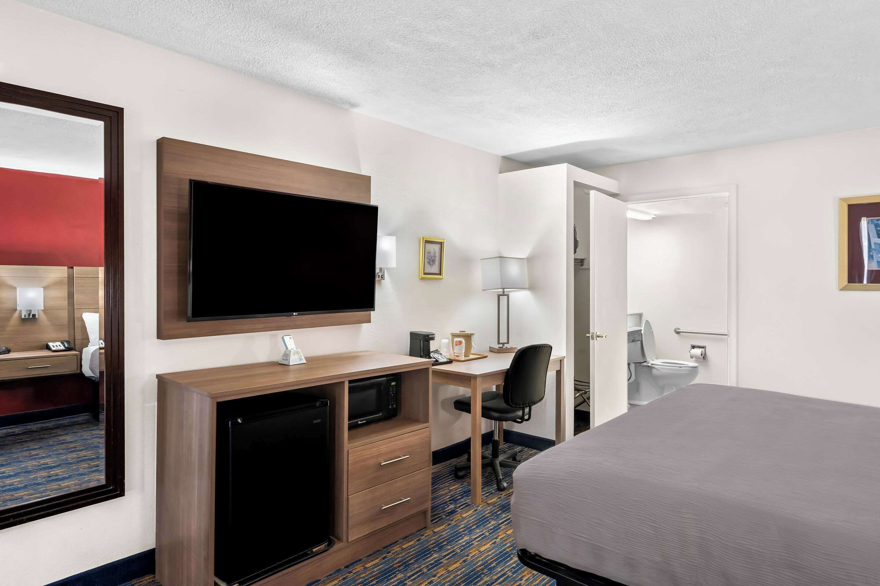 A hotel room with a bed, a desk with a computer, a television, a microwave, and a small refrigerator.
