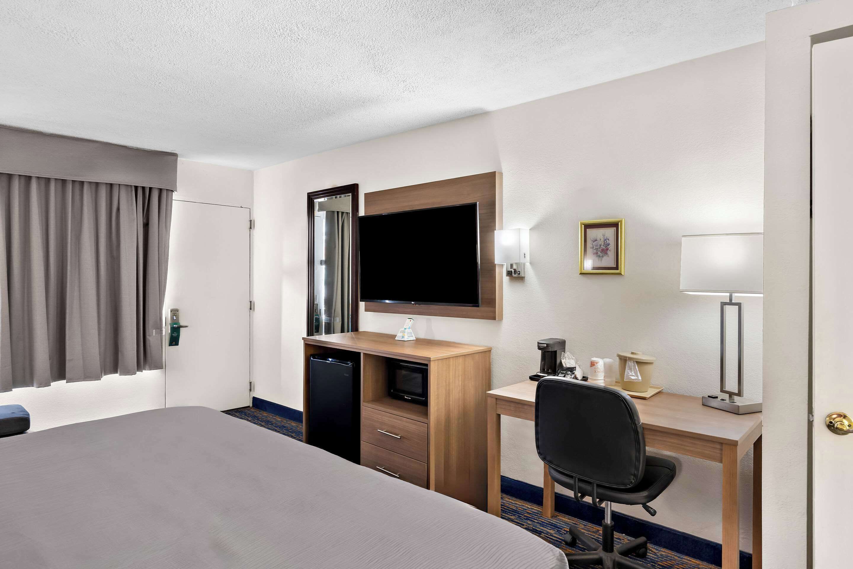 A hotel room with a bed, desk, chair, television, and a small kitchenette.