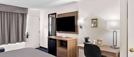 Une chambre d’hôtel équipée d’un lit, d’un bureau, d’une chaise, d’une télévision et d’une petite kitchenette.