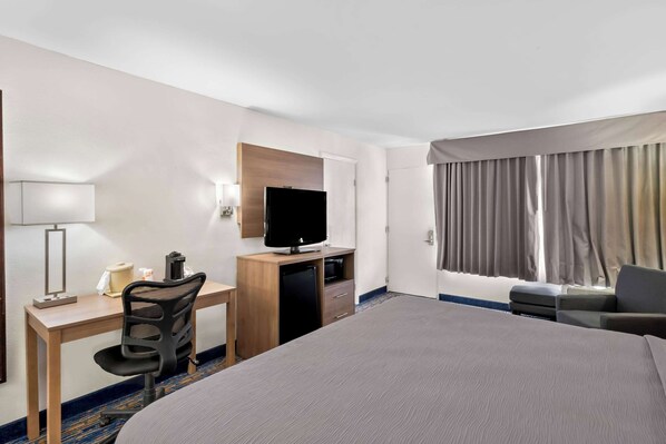 Habitación de hotel con una cama grande, un escritorio con computadora, televisión y ventana con cortinas.