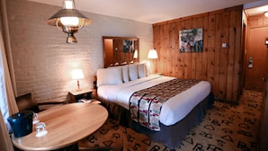 A hotel room with a wooden bed, a round wooden table, a lamp, and a painting on the wall. - Dude Rancher Lodge (Billings)
