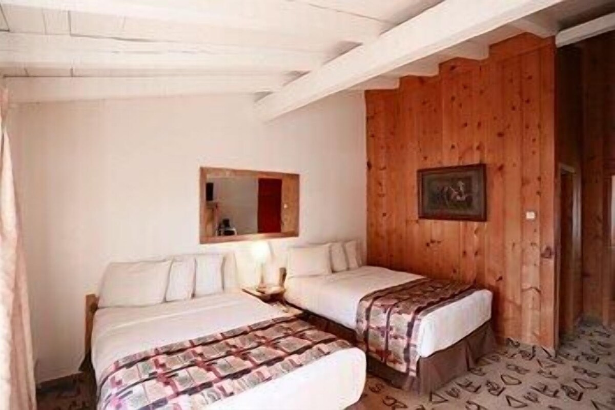 A room with two beds, a wooden wall, a mirror, and a framed picture.