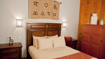 A bedroom with a wooden headboard, a bed with white bedding, a red patterned throw, a wooden nightstand, a small table, and a wooden wardrobe.