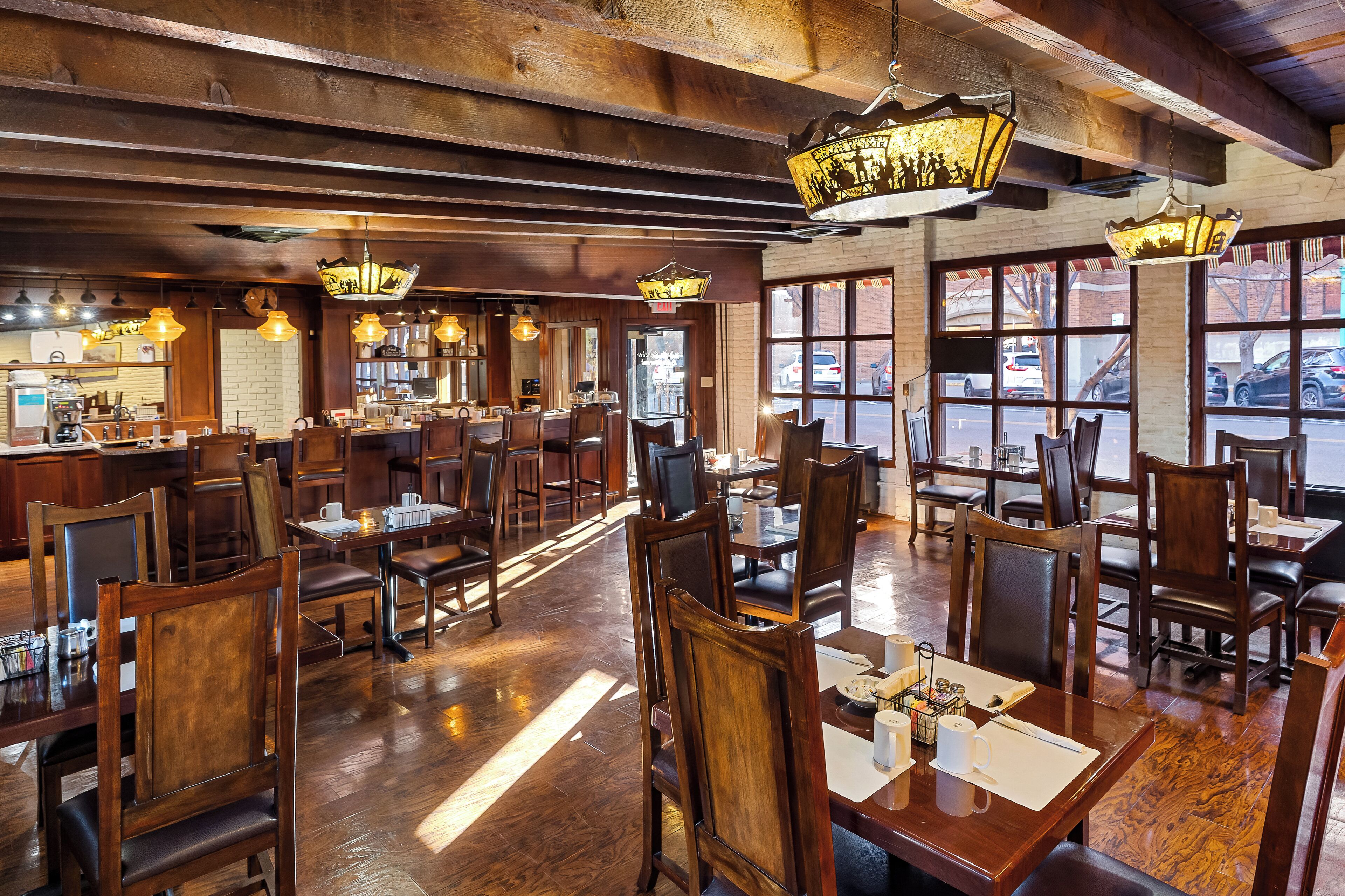 Een restaurantinterieur met houten meubels, hangende lampen en grote ramen.