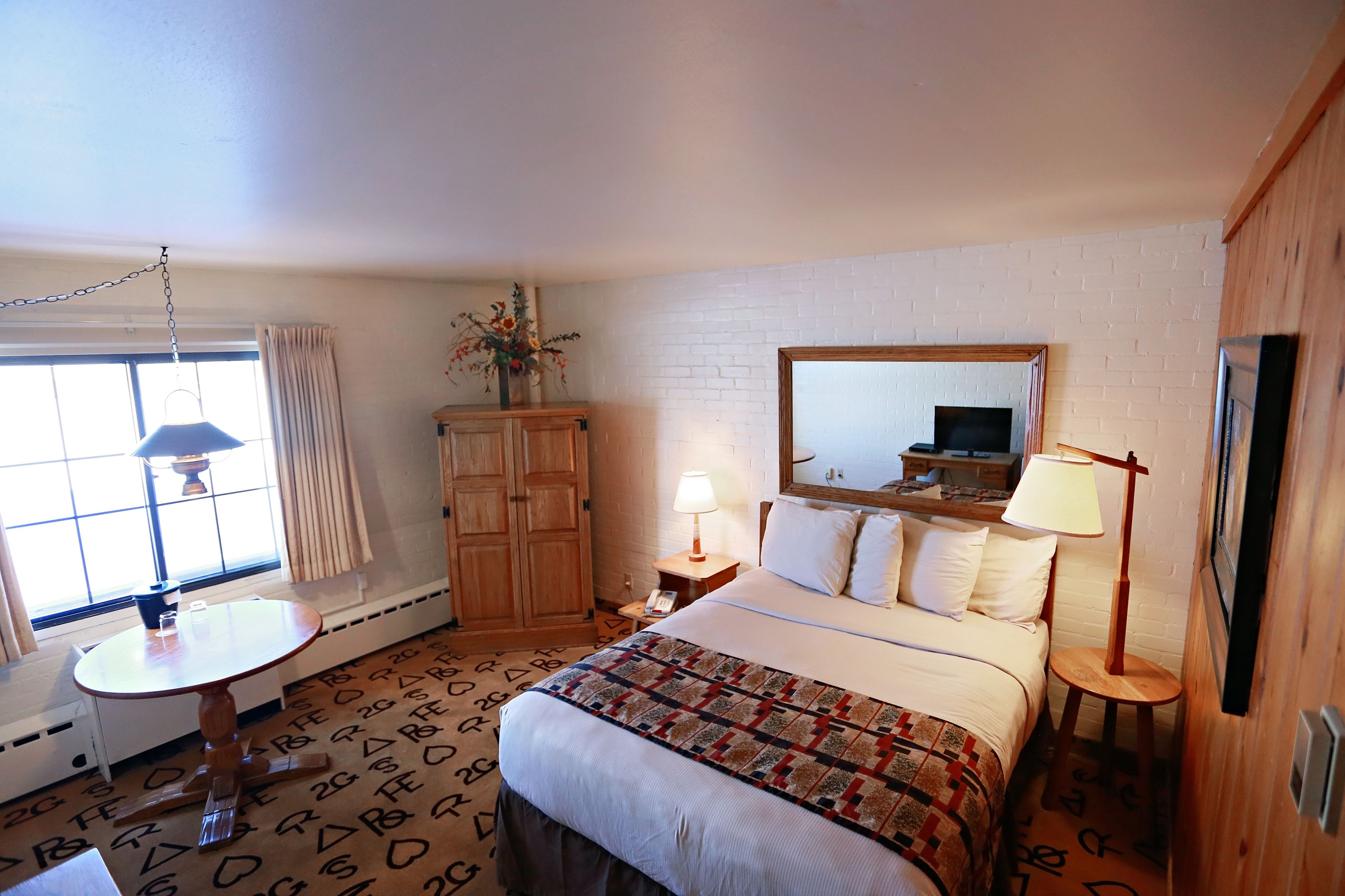 Une chambre d’hôtel équipée d’un lit, d’un bureau, d’une chaise, d’une lampe, d’un miroir et d’une fenêtre avec des rideaux.