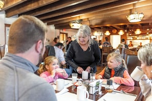 A group of people seated at a table in a restaurant with wooden beams on the ceiling and hanging lights. - Dude Rancher Lodge (Billings)