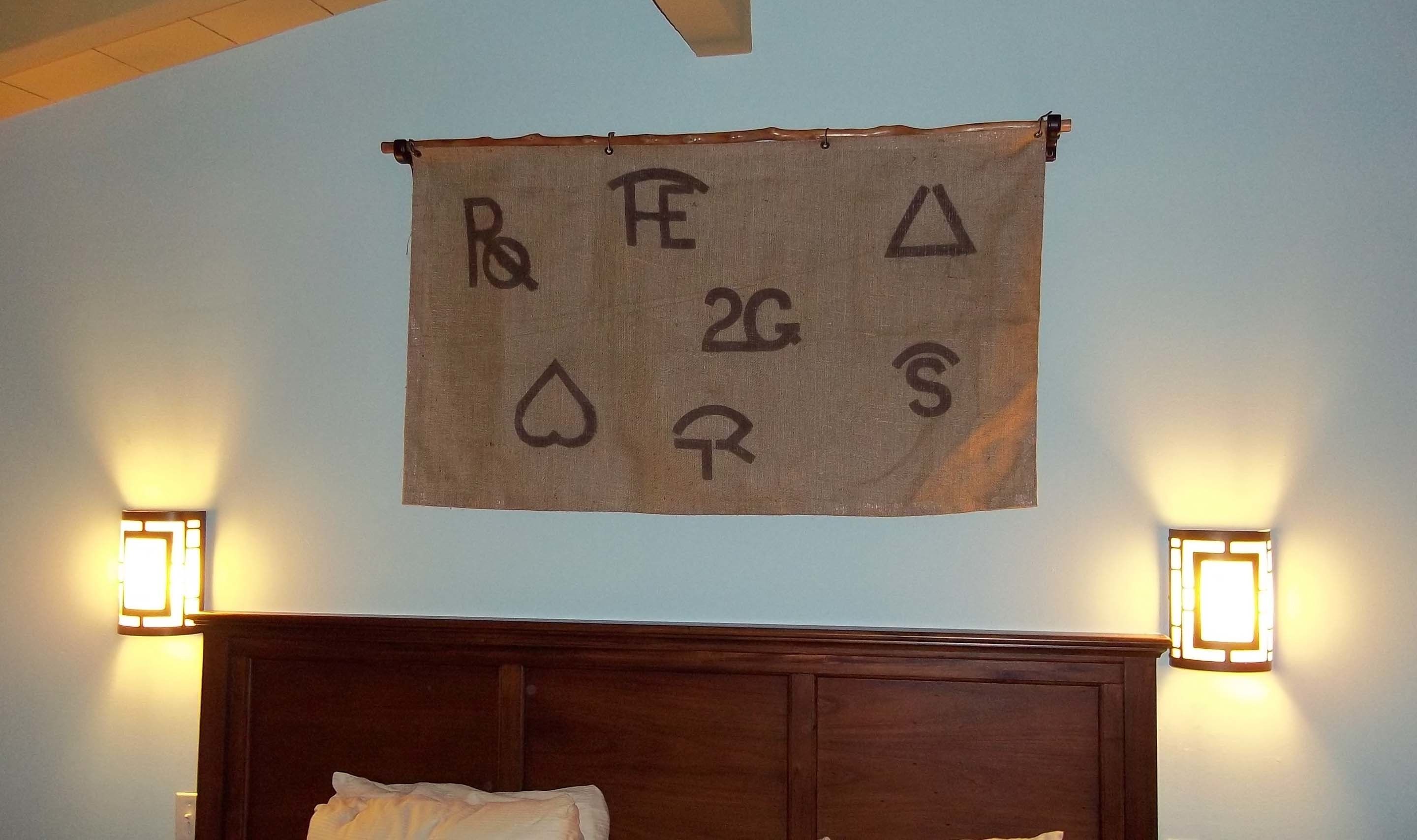 A room with a wooden headboard, two wall-mounted light fixtures, and a hanging tapestry with symbols.