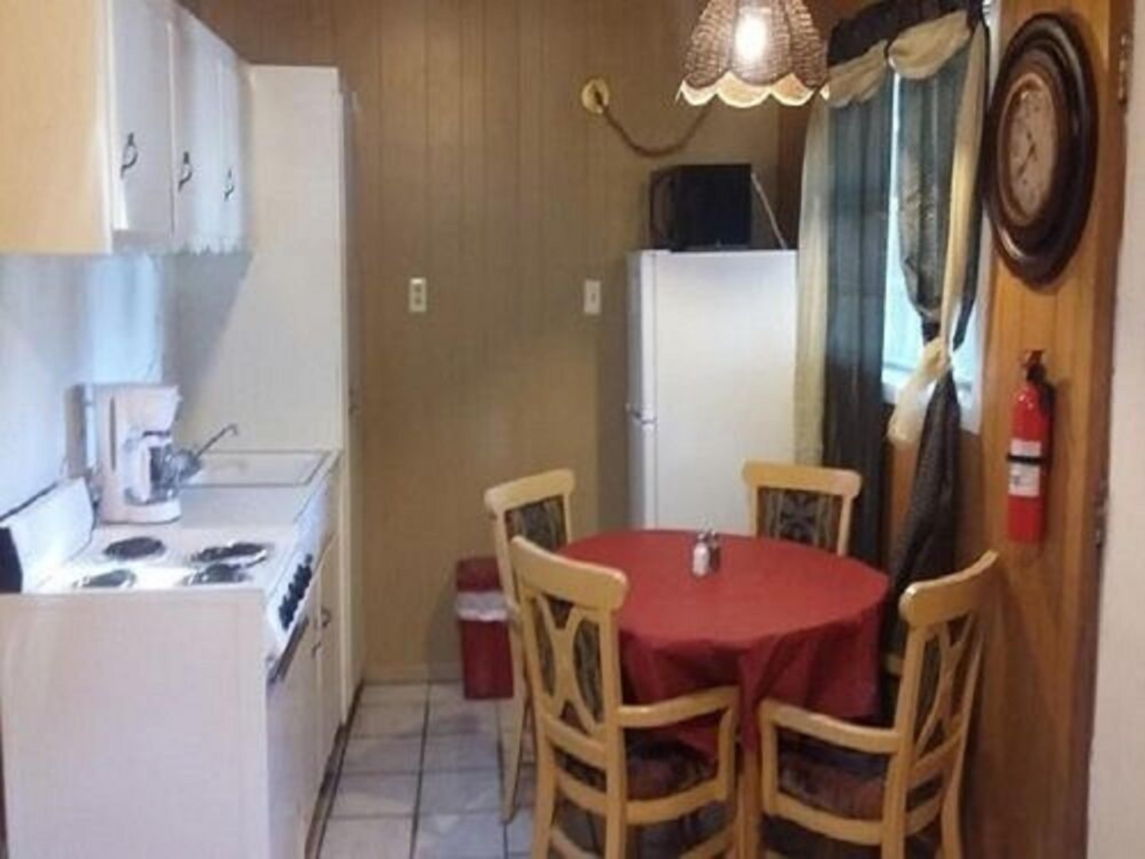 Una cocina compacta con estufa, cafetera y mesa de comedor con cuatro sillas.