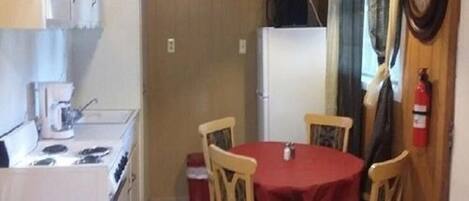 Una cocina compacta con estufa, cafetera y mesa de comedor con cuatro sillas.