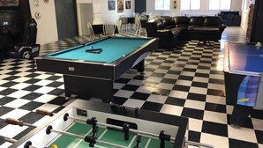 Ein Billardtisch, ein Kicker und ein Snookertisch in einem Raum mit Schachbrettmuster und einer Couch.