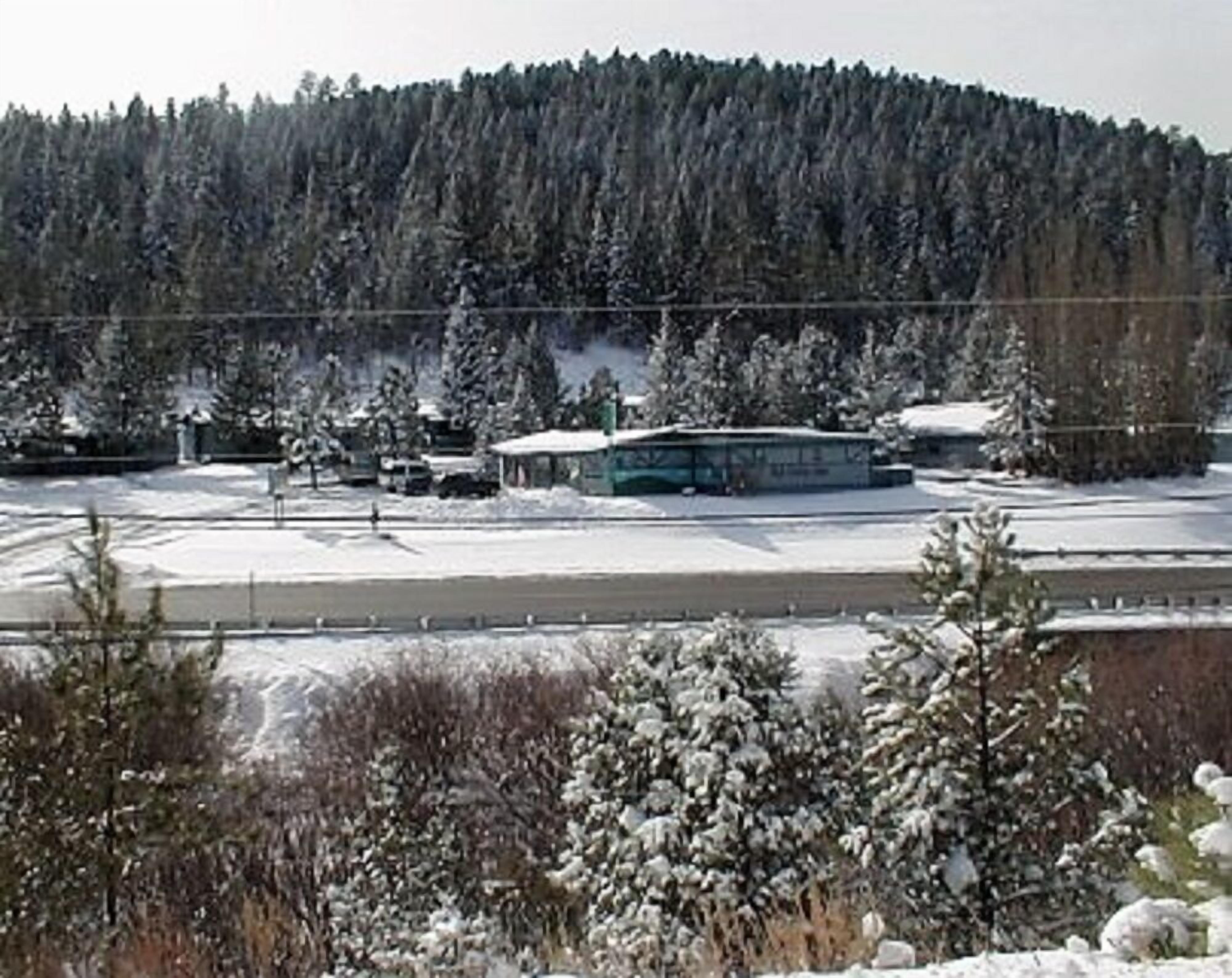 Paisaje nevado con un edificio que parece un hotel o centro turístico, rodeado de árboles y una colina boscosa.