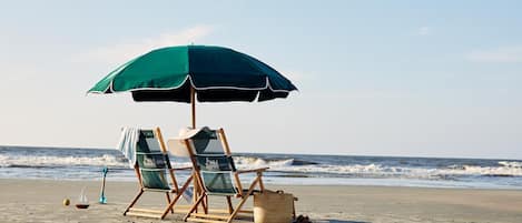 Two beach chairs under a green umbrella on a sandy beach with the ocean in the background.