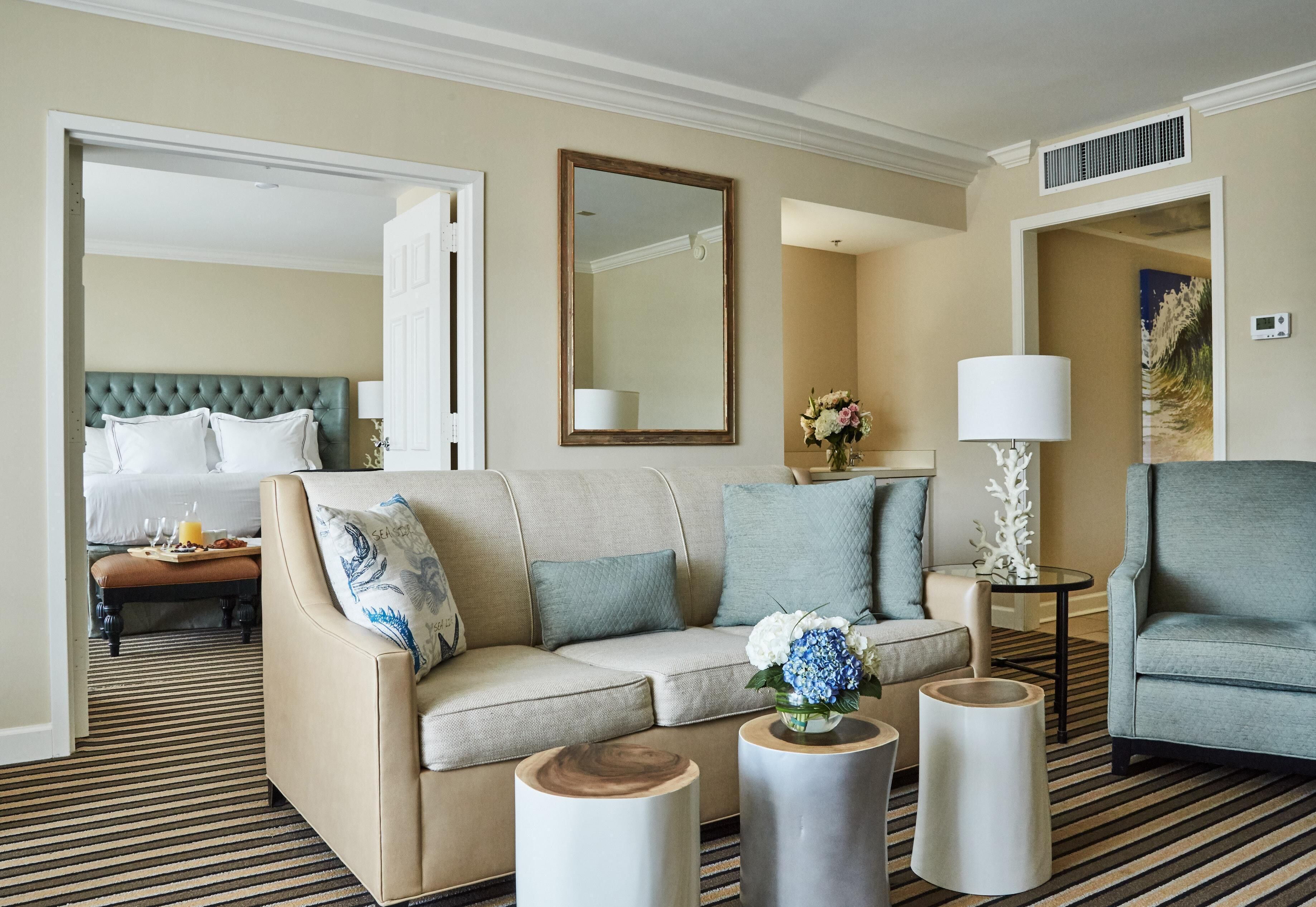 A hotel room with a sofa, a coffee table, a side table, a chair, a bed, and a mirror.