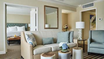 A hotel room with a sofa, a coffee table, a side table, a chair, a bed, and a mirror.