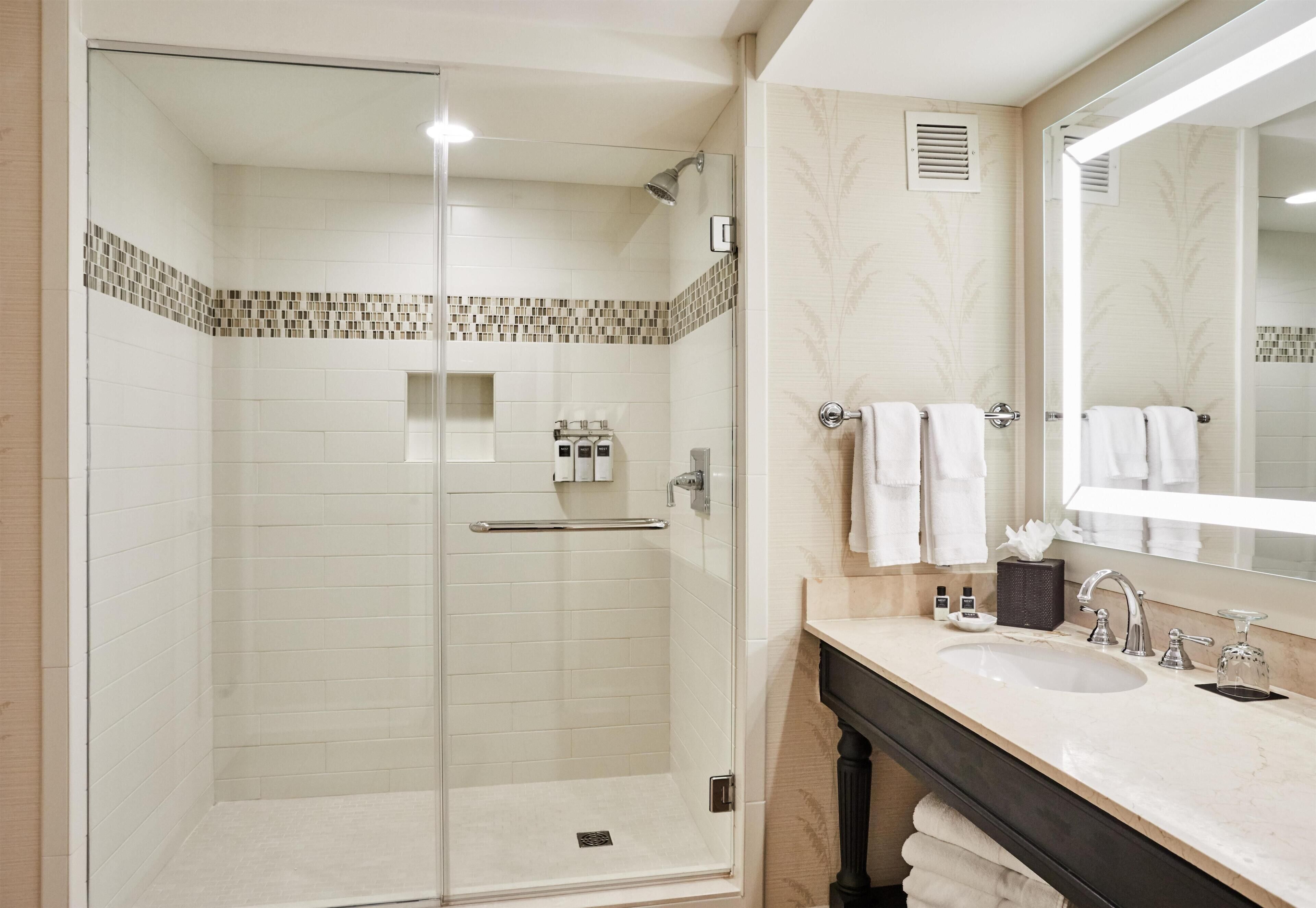 A modern bathroom with a glass-enclosed shower, a vanity with a sink, and a large mirror.