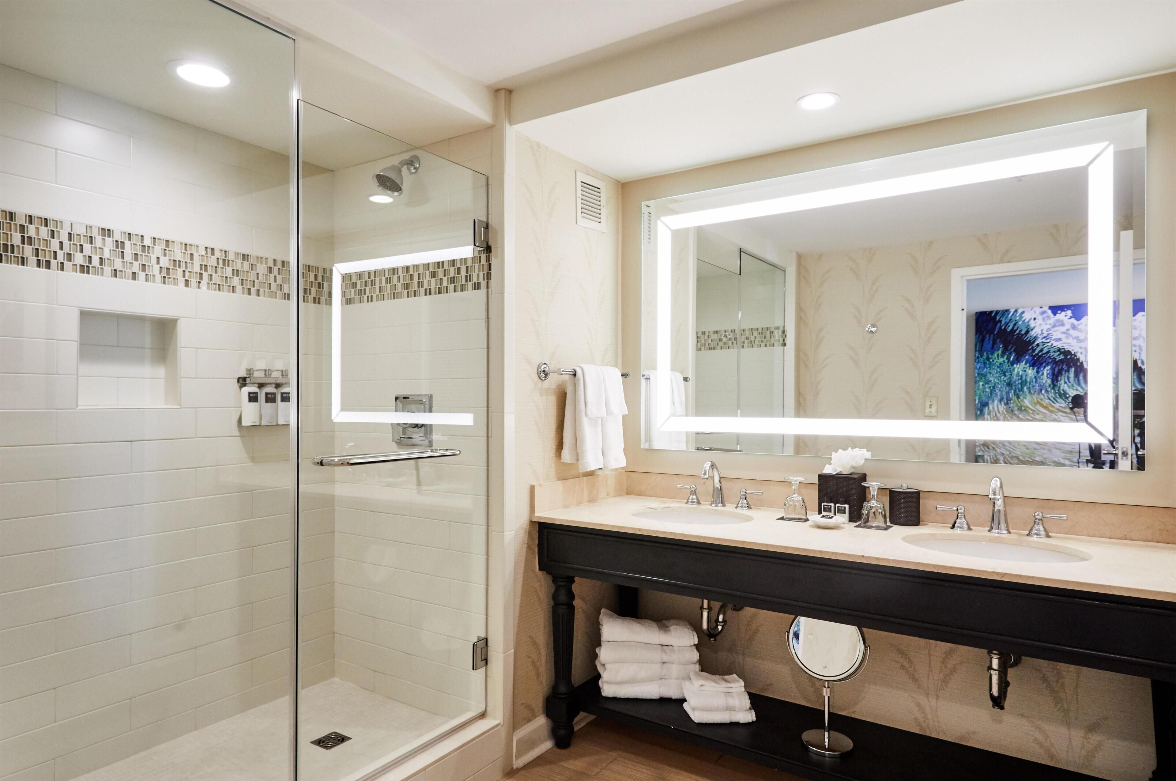A modern bathroom with a glass-enclosed shower, a vanity with a large mirror, and a sink with multiple faucets.