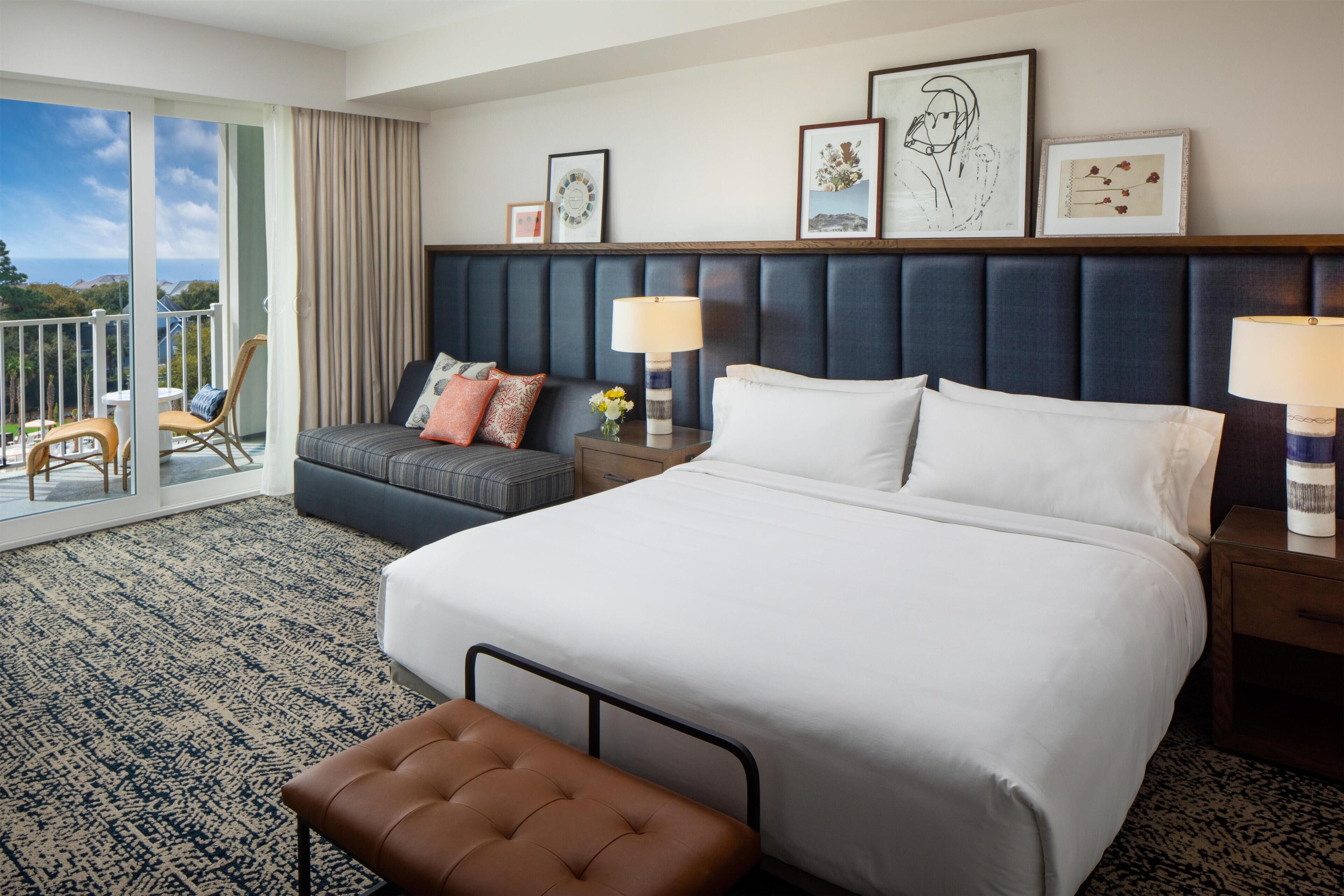Hotelkamer met een groot bed, een sofa, een fauteuil en een balkon met uitzicht.
