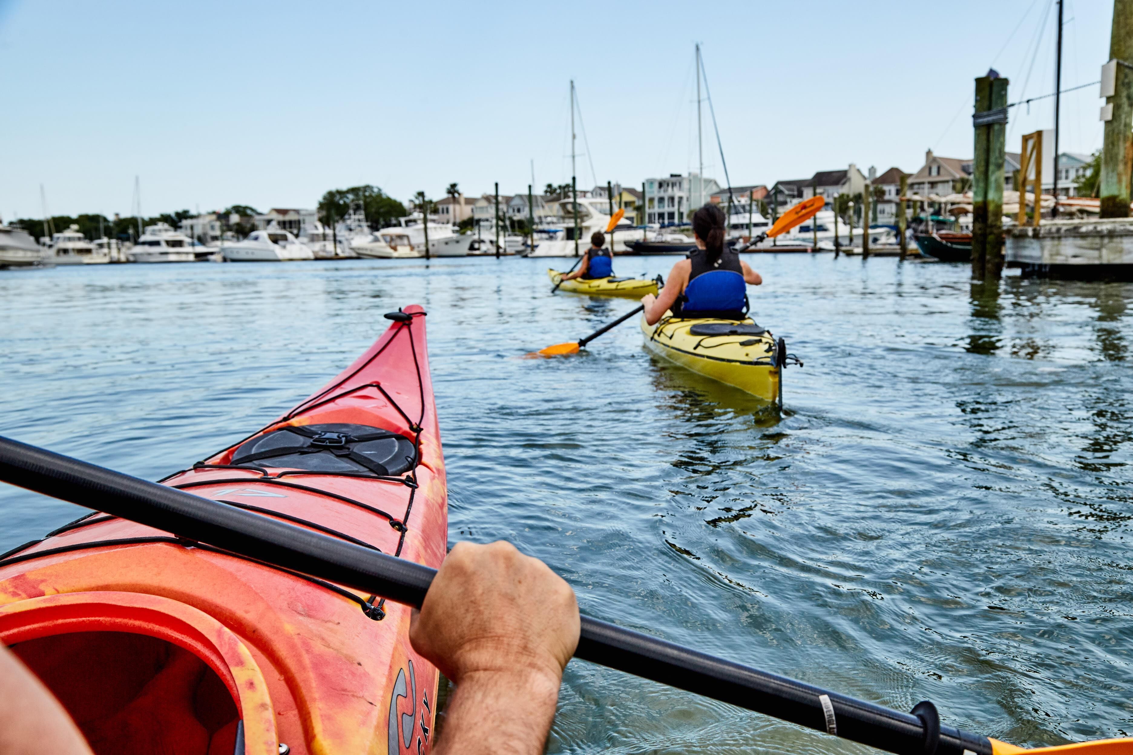 A person in a red kayak on a calm body of water with other kayaks in the background.