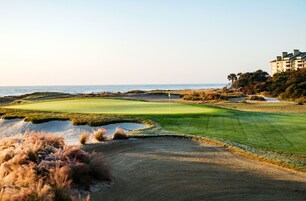 A golf course with bunkers, a sand trap, and a building in the background.