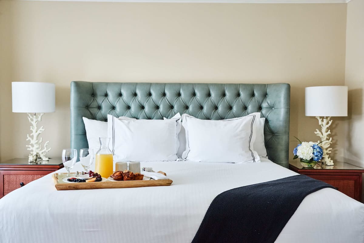 A neatly made bed with a tufted headboard, white linens, and a tray with breakfast items.