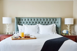 A neatly made bed with a tufted headboard, white linens, and a tray with breakfast items.