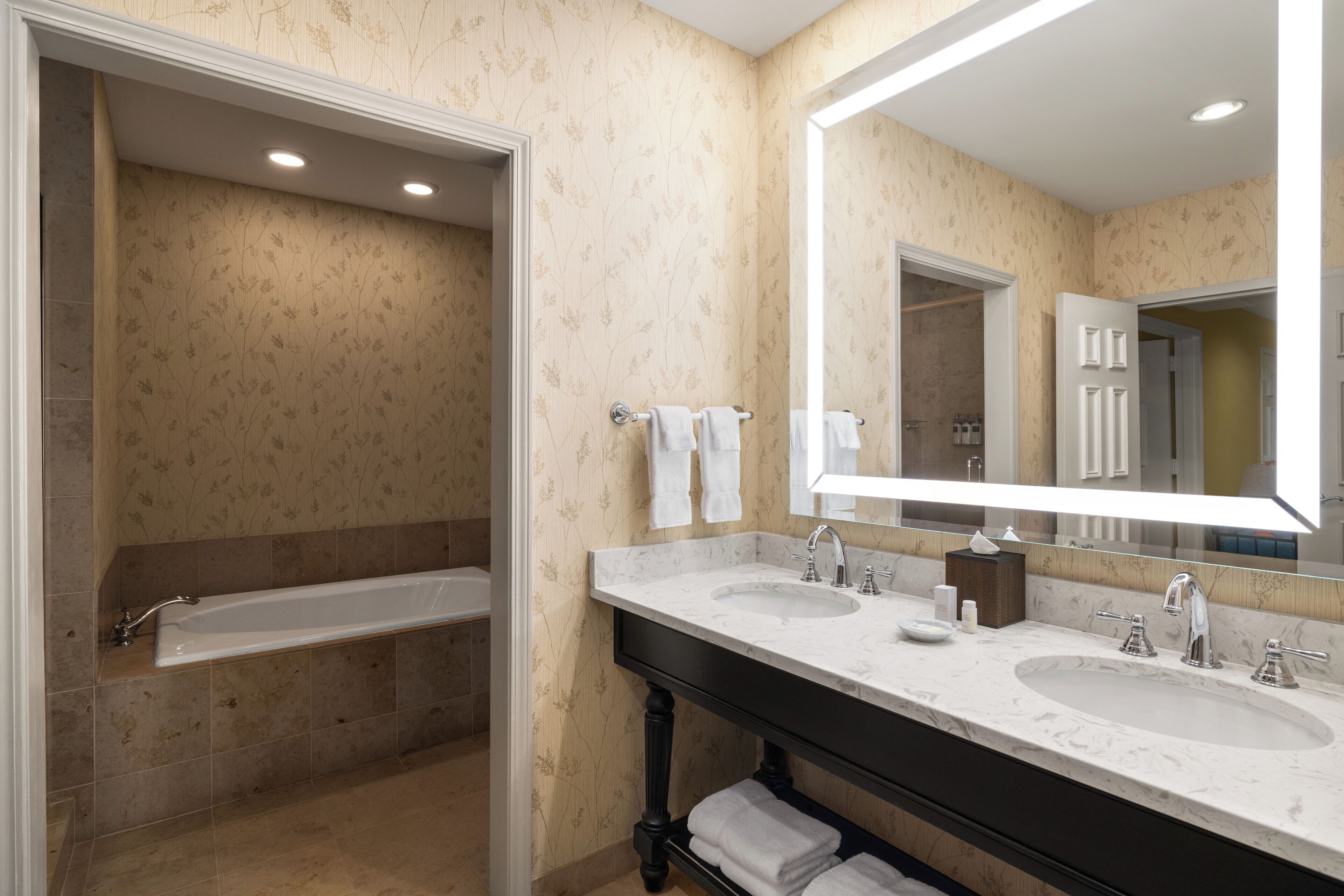 A modern bathroom with two sinks, a large mirror, and a bathtub.