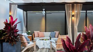 A modern outdoor seating area with a sofa, chairs, and a table, surrounded by large windows and curtains.