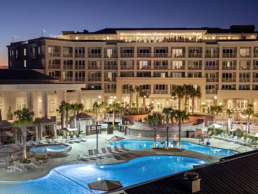 Un hotel con varias piscinas, zonas de estar al aire libre y un edificio grande con balcones.