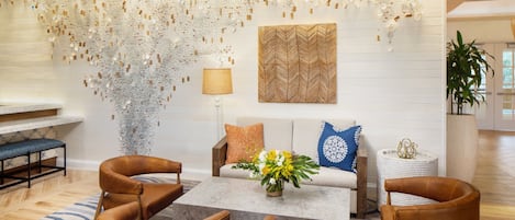 A modern living room with a sofa, two brown leather chairs, a coffee table, and a decorative wall with hanging elements.