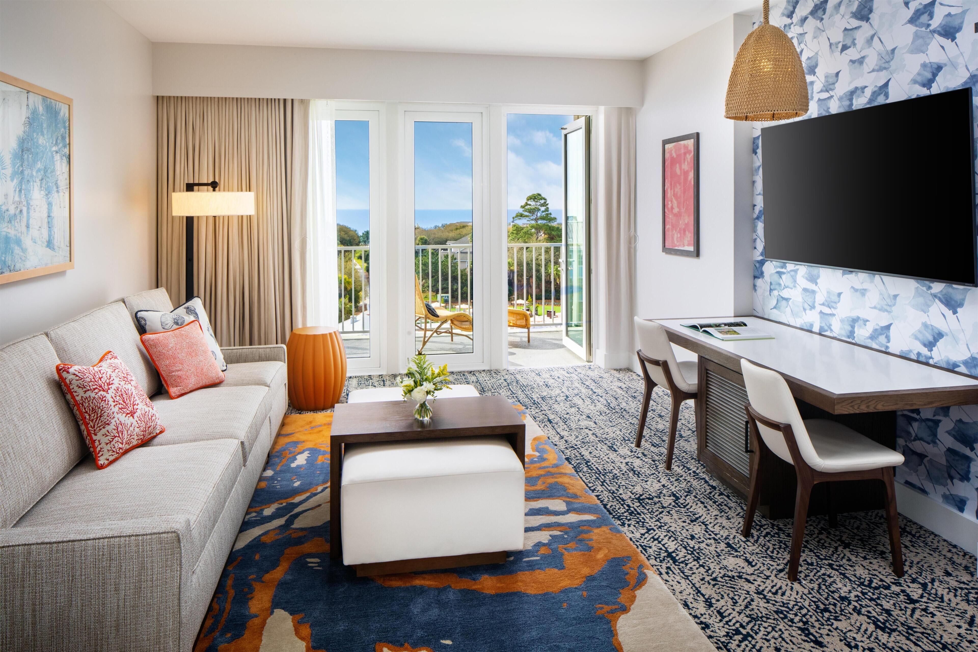 Quarto de hotel moderno com sofá, mesa de centro, espaço de refeições e varanda com vista.