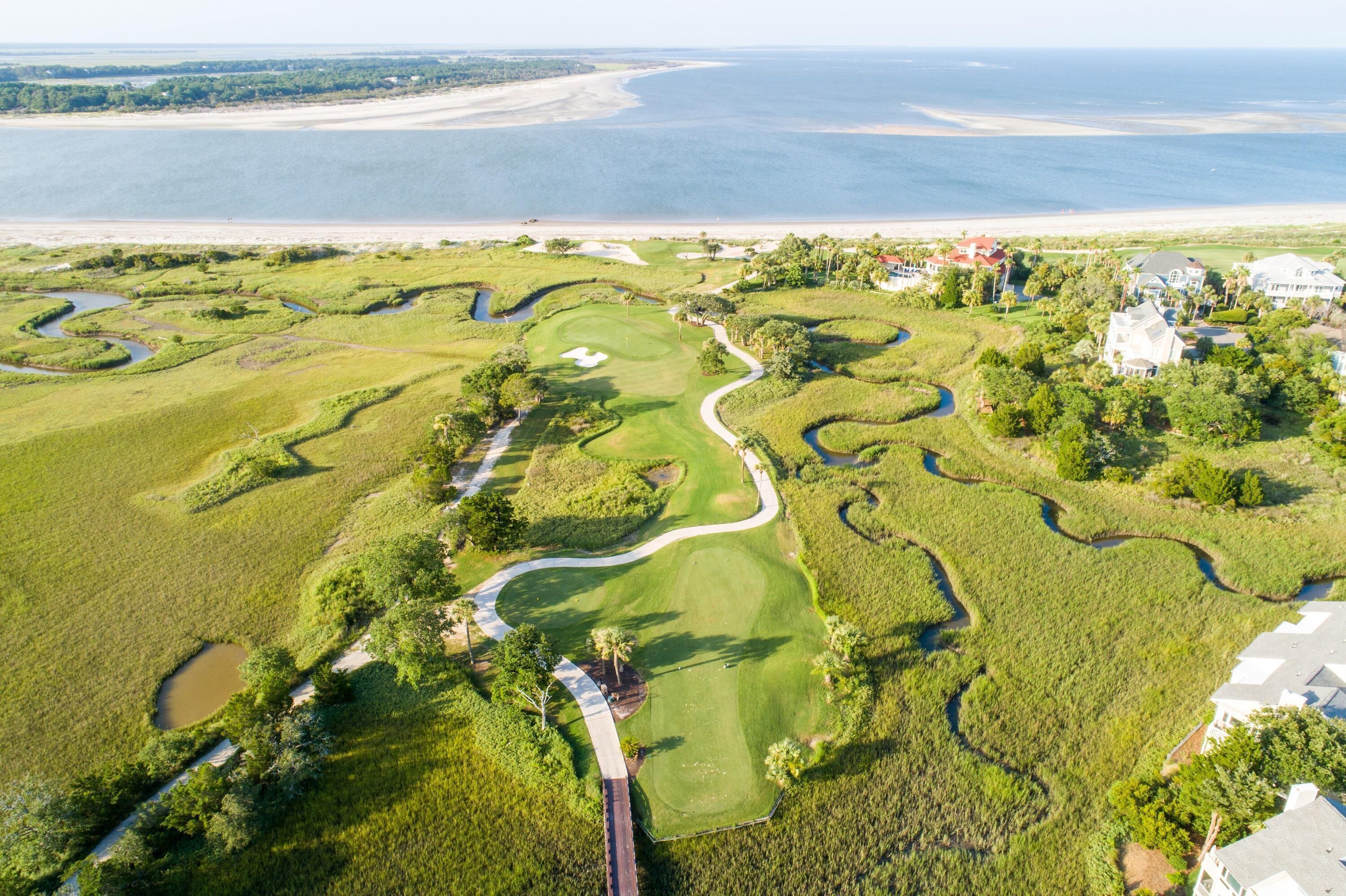 An aerial view of a golf course with a water body in the background, surrounded by residential properties.