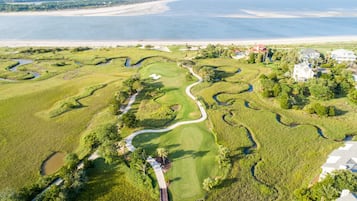 An aerial view of a golf course with a water body in the background, surrounded by residential properties.