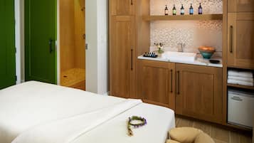 A bedroom with a bed, a green door, a wooden cabinet with toiletries, and a small sink.