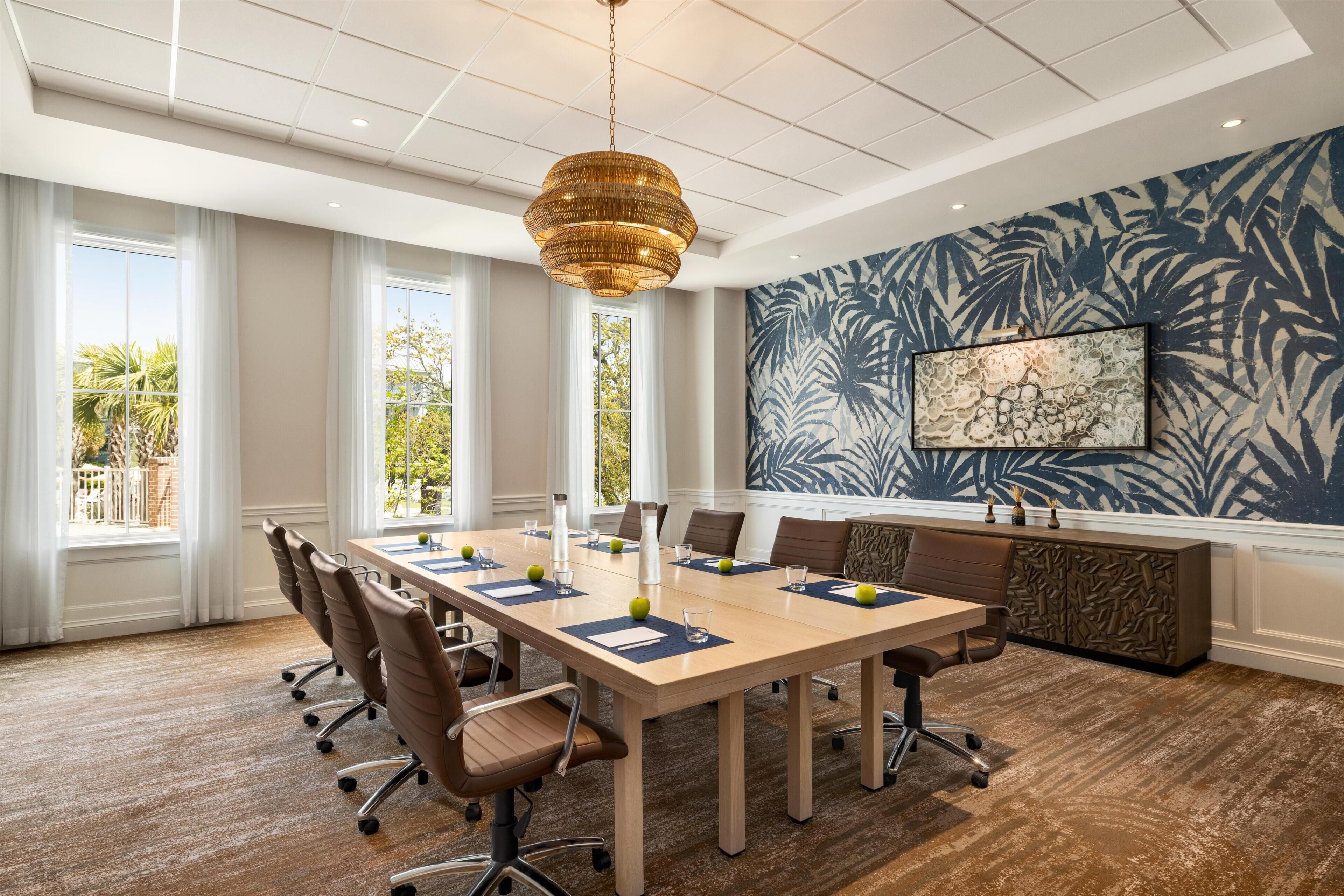 A conference room with a long table, chairs, a decorative wall, and a ceiling light.