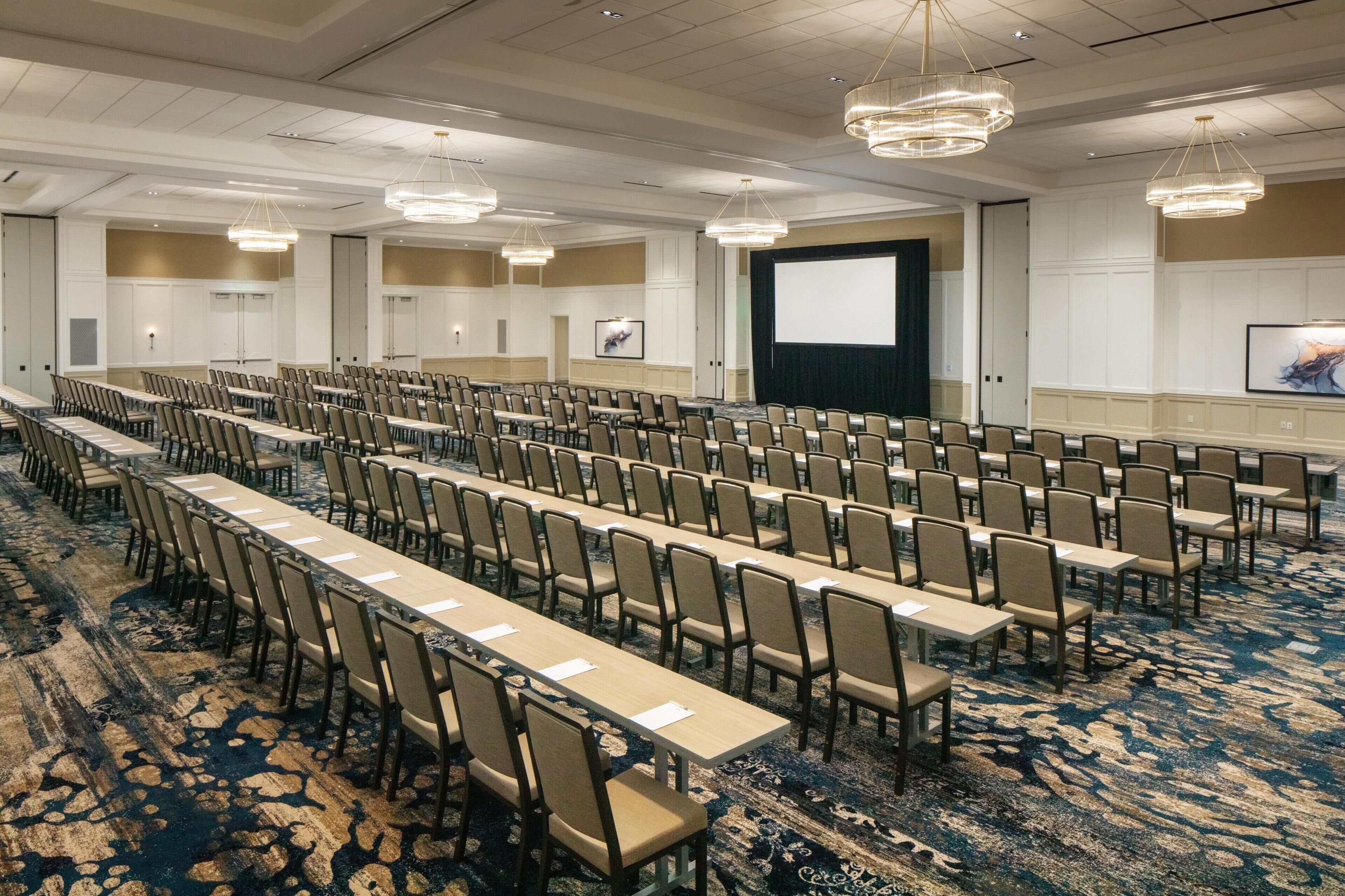 A conference room with rows of tables and chairs, a large screen, and a projector.