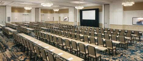 A conference room with rows of tables and chairs, a large screen, and a projector.
