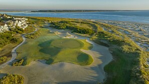 A golf course with a sandy central area, a water body, and a residential area with houses in the background.