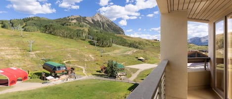 A balcony with a mountain view, a red tent-like structure, and a green-roofed building.