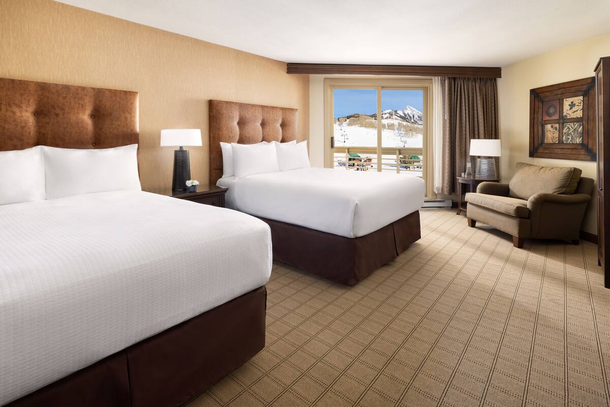 A hotel room with two large beds, a sofa, a window with a view of mountains, and a painting on the wall.