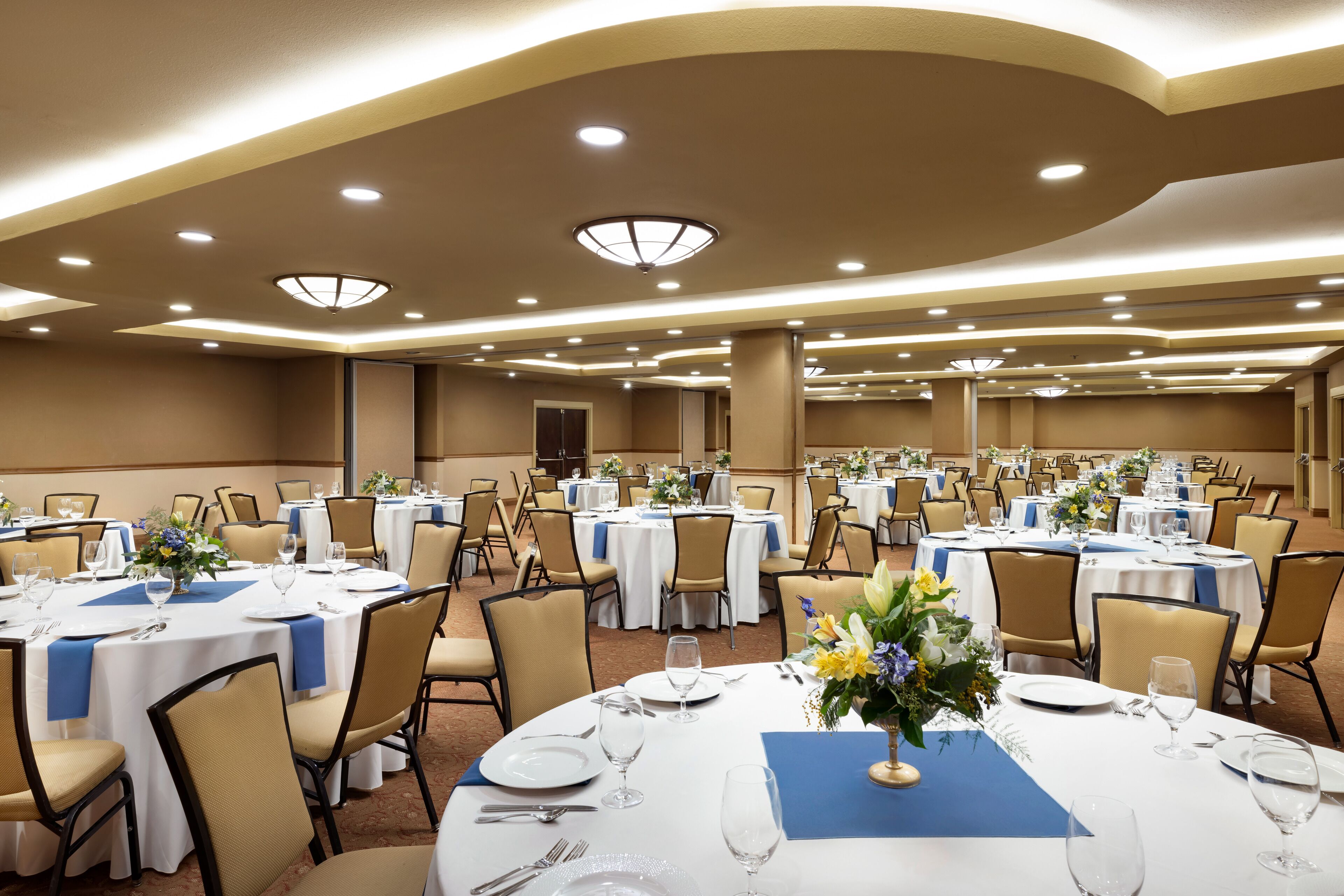 Une salle de banquet avec des tables rondes, des chaises de couleur beige et des nappes blanches.