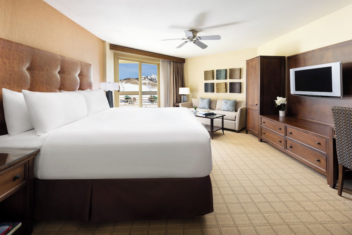 A hotel room with a large bed, a television, a desk, and a view of the mountains.