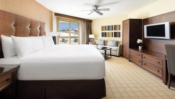 A hotel room with a large bed, a television, a desk, and a view of the mountains.