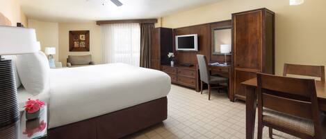 A hotel room with a large bed, a desk with a computer, a TV, and a ceiling fan.