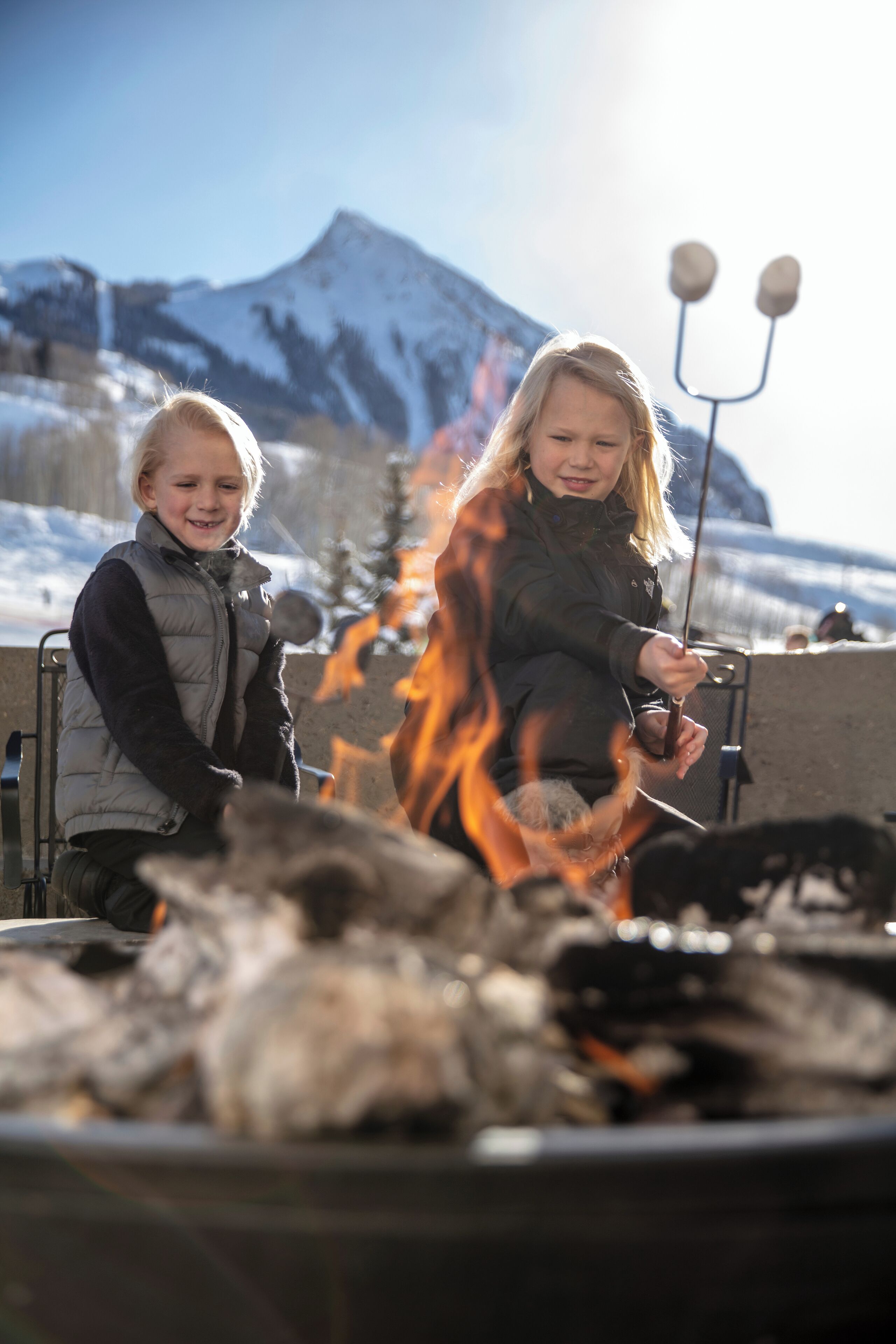 Two people roasting marshmallows over a campfire with a mountain in the background.