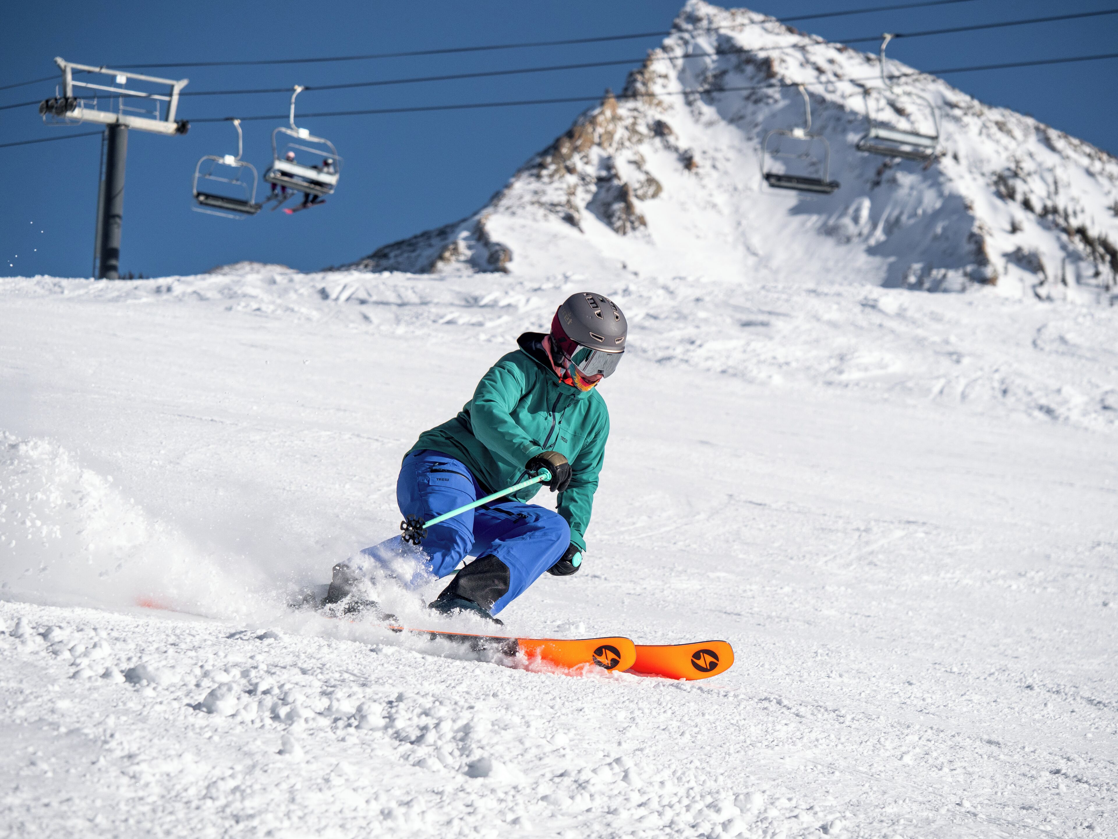 A person skiing down a snowy slope with ski lifts in the background.