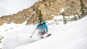 Une personne fait du ski sur une pente enneigée, avec des montagnes rocheuses en arrière-plan.